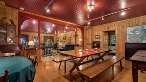 Un intérieur rustique en bois, avec une grande table et des bancs en bois, des murs en bois et un plafond avec des poutres apparentes et des luminaires.