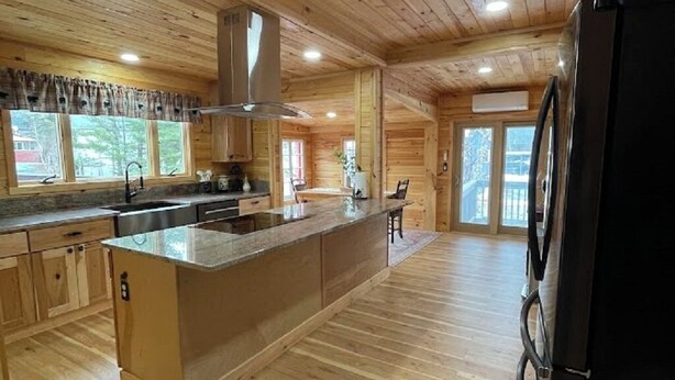 Une cuisine spacieuse avec un plancher en bois, un îlot central et un réfrigérateur noir.