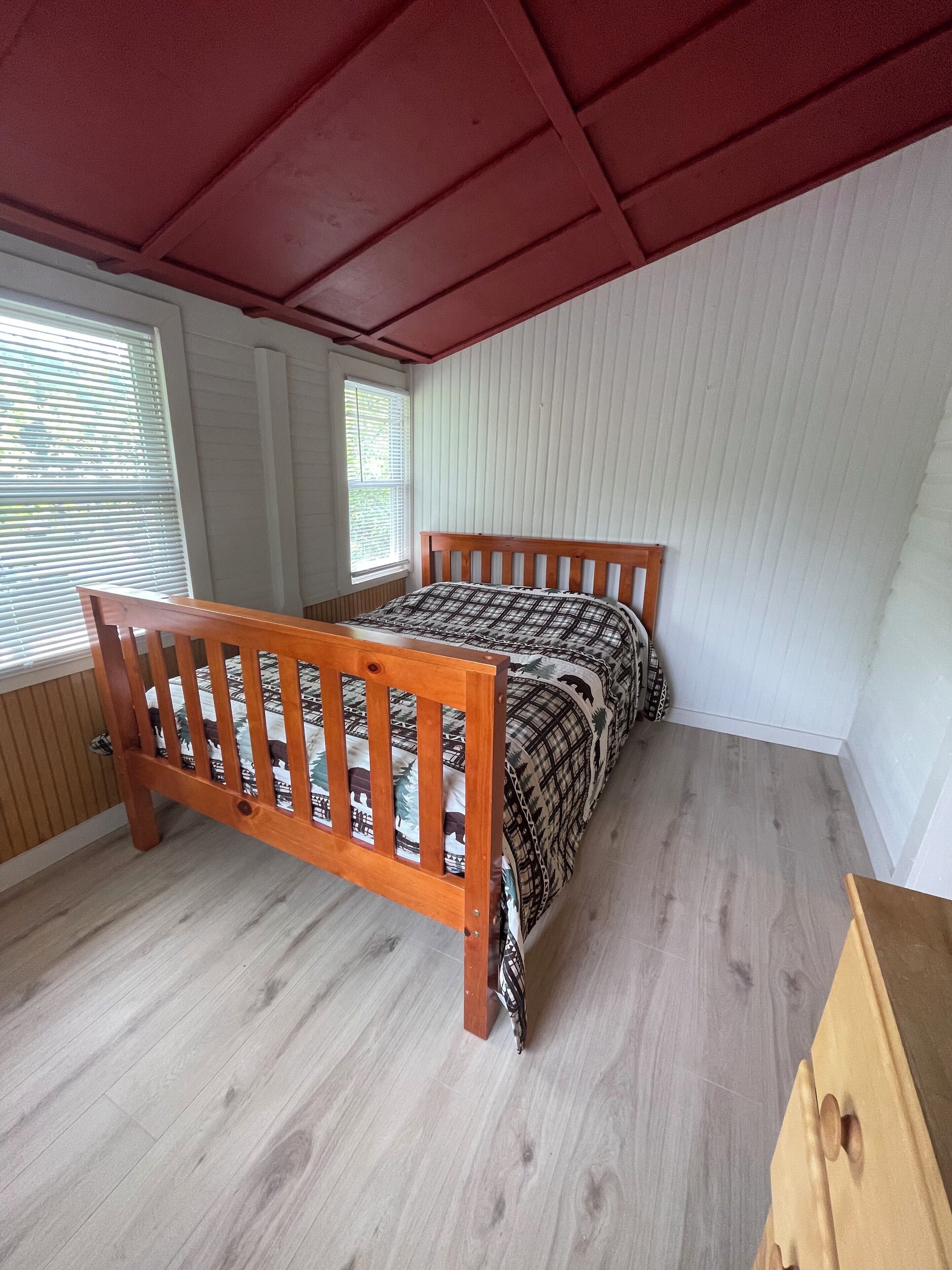 A bedroom with a wooden bed, a window with blinds, and a red ceiling.