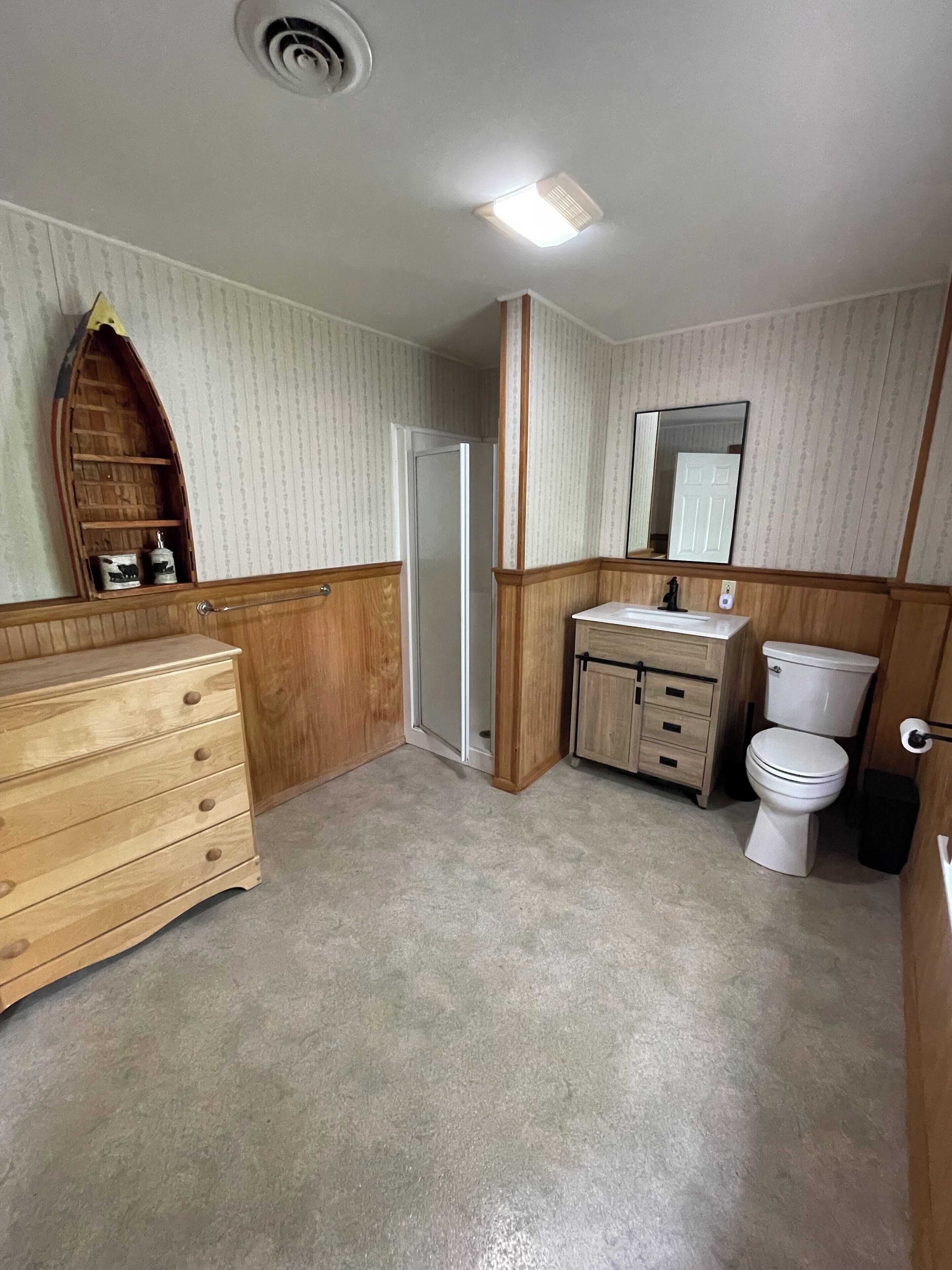 Une salle de bain avec un meuble-lavabo en bois, des toilettes et une douche.