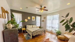 A bedroom with a bed, a ceiling fan, a wooden floor, and large windows.