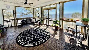 A sunroom with a large view of the sea, a ceiling fan, and a round patterned rug.