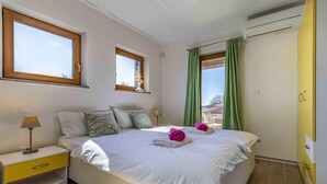 Un dormitorio con cama, mesita de noche, lámpara y ventana con cortinas.