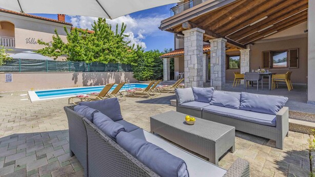 Un patio exterior con piscina, sillas de descanso y una zona de estar cubierta.