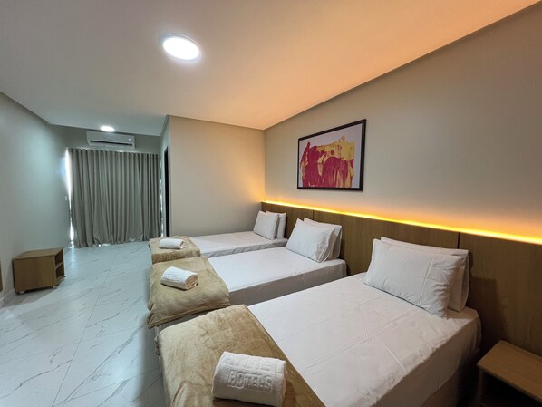Une chambre d’hôtel avec deux lits, une grande fenêtre avec des rideaux, un luminaire au plafond et un tableau accroché au mur.