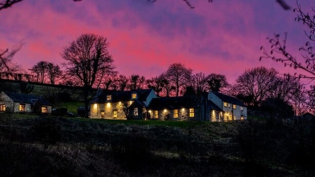 A large, multi-story house with multiple lit windows, surrounded by trees and set against a twilight sky. - Meadow Sweet, Meadowsweet Cottage Jacuzzi Edition (Saundersfoot)