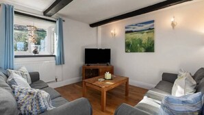 A living room with a wooden coffee table, grey sofas, a TV on a stand, and a painting on the wall. - Meadow Sweet, Meadowsweet Cottage Jacuzzi Edition (Saundersfoot)
