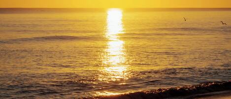 A sunset over a calm sea with the sun reflecting on the water.