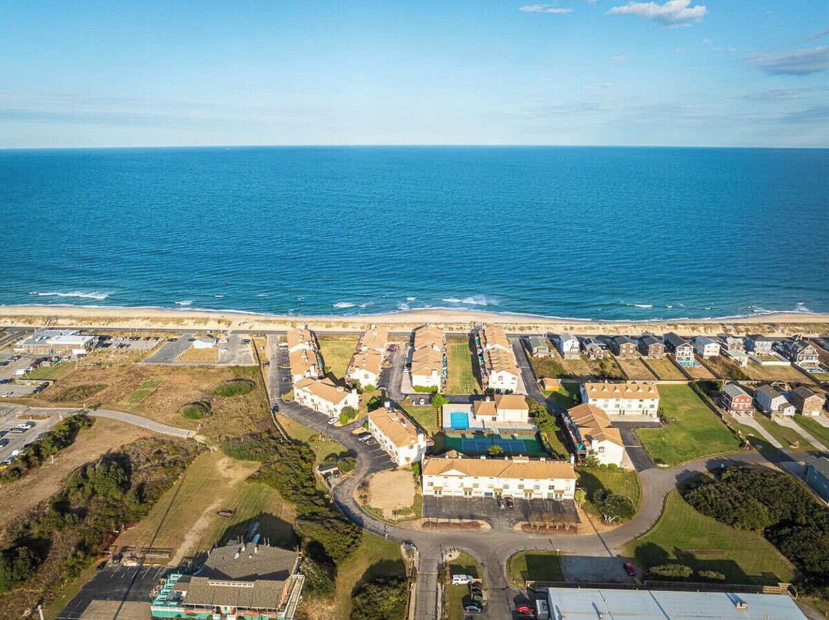 Vue aérienne d’une zone résidentielle côtière, avec des maisons, des routes et une plage.