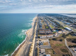An aerial view of a coastal town with a beachfront, residential buildings, and a mix of commercial properties.