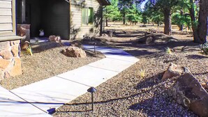 A house with a stone foundation, a covered porch, and a landscaped yard with rocks and trees. - 3 Amigos-golf, canyon, RV garage (Williams)