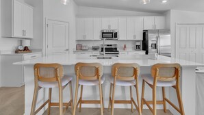 A modern kitchen with white cabinetry, a central island with bar stools, a microwave, a coffee maker, and a refrigerator. - 2 bed 2 bath GOLF condo in Webbs Reserve (Punta Gorda)