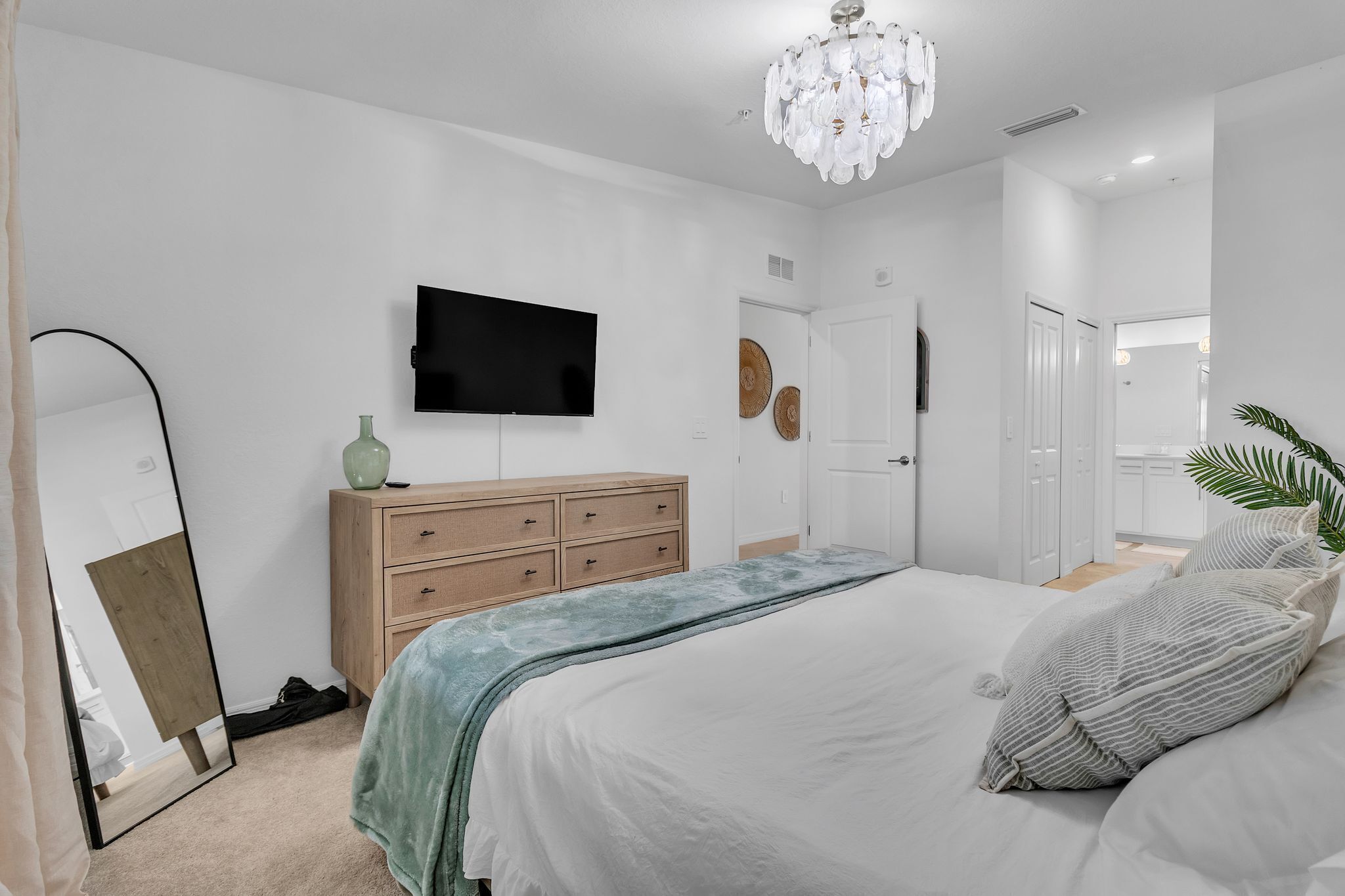 A bedroom with a bed, a dresser, a TV, a mirror, and a chandelier.