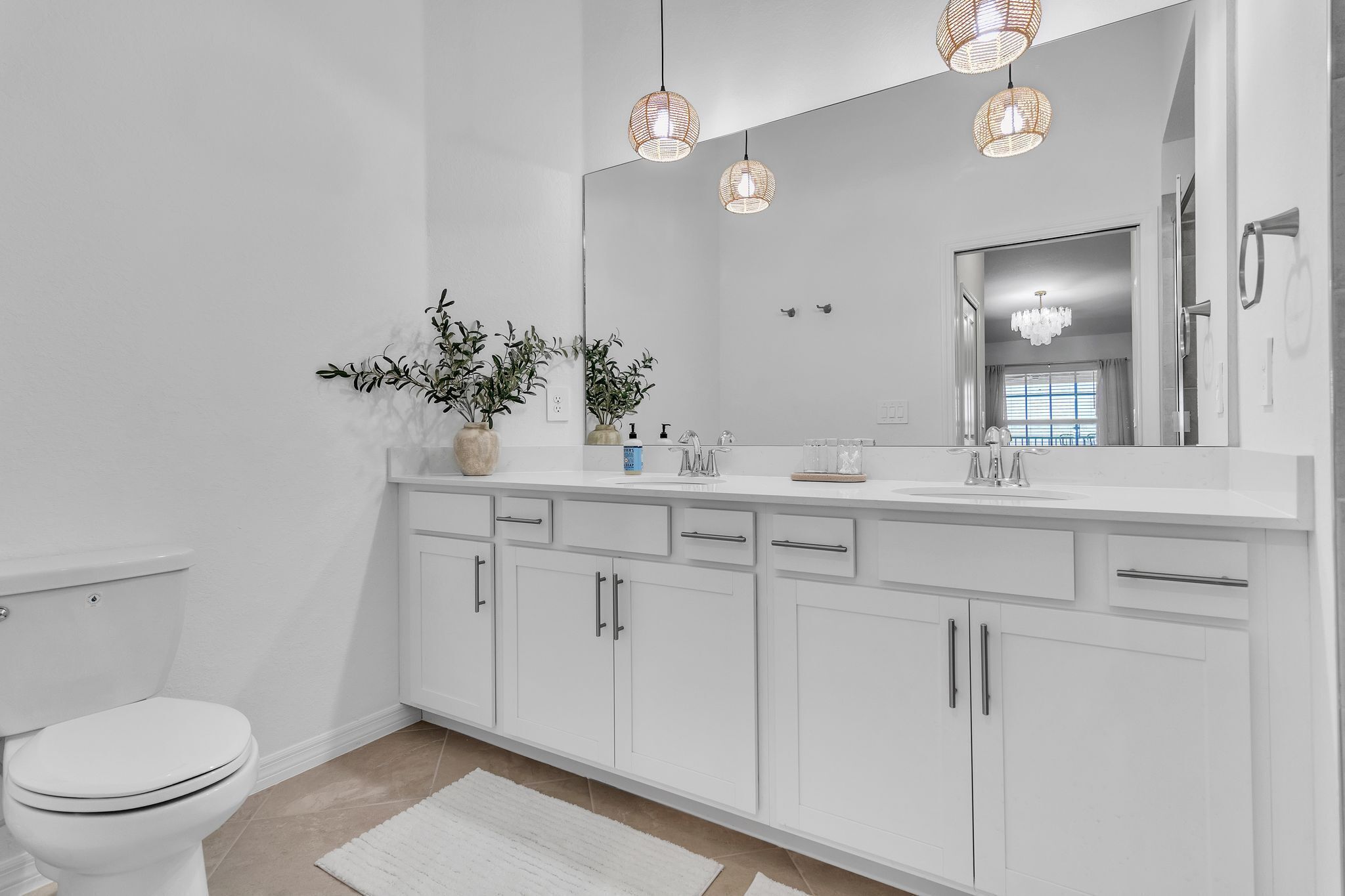 A modern bathroom with white cabinetry, a large mirror, and two pendant lights.