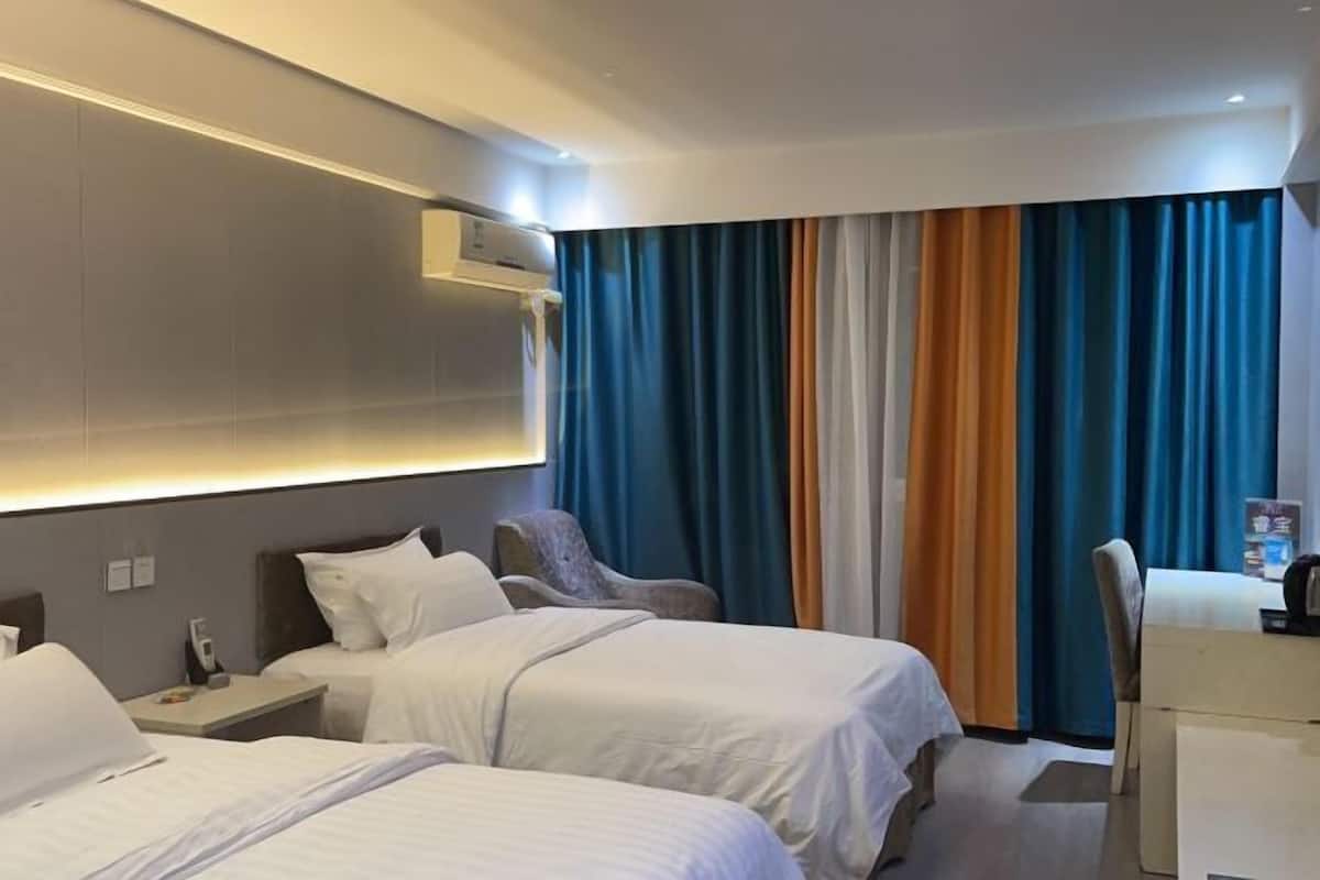 A hotel room with two beds, a desk, and a chair. There is an air conditioning unit on the wall and a curtain with multiple colors.