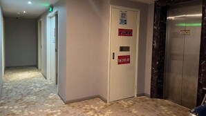 Un pasillo de hotel con piso estampado, una puerta con un letrero rojo y un ascensor con paneles de mármol.