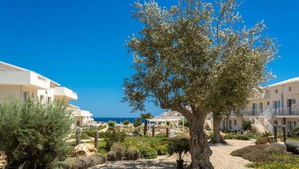 Een hotel in mediterrane stijl met een centrale binnenplaats met bomen, terrasplekken en uitzicht op zee.