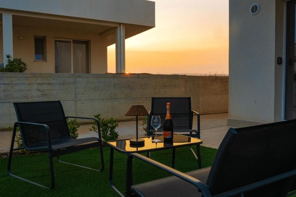 Une terrasse avec deux chaises, une table, une bouteille de vin et un verre.