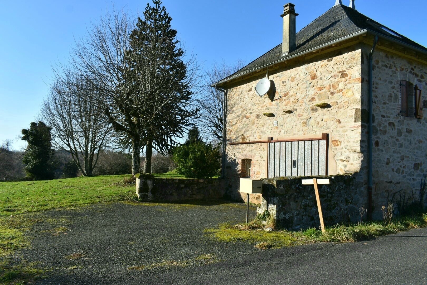 A stone building with a metal gate, a clear sky, and a grassy field.
