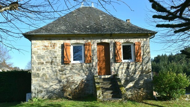 Ein Haus aus Stein mit einem steilen Dach, hölzernen Fensterläden und einer kleinen Veranda.