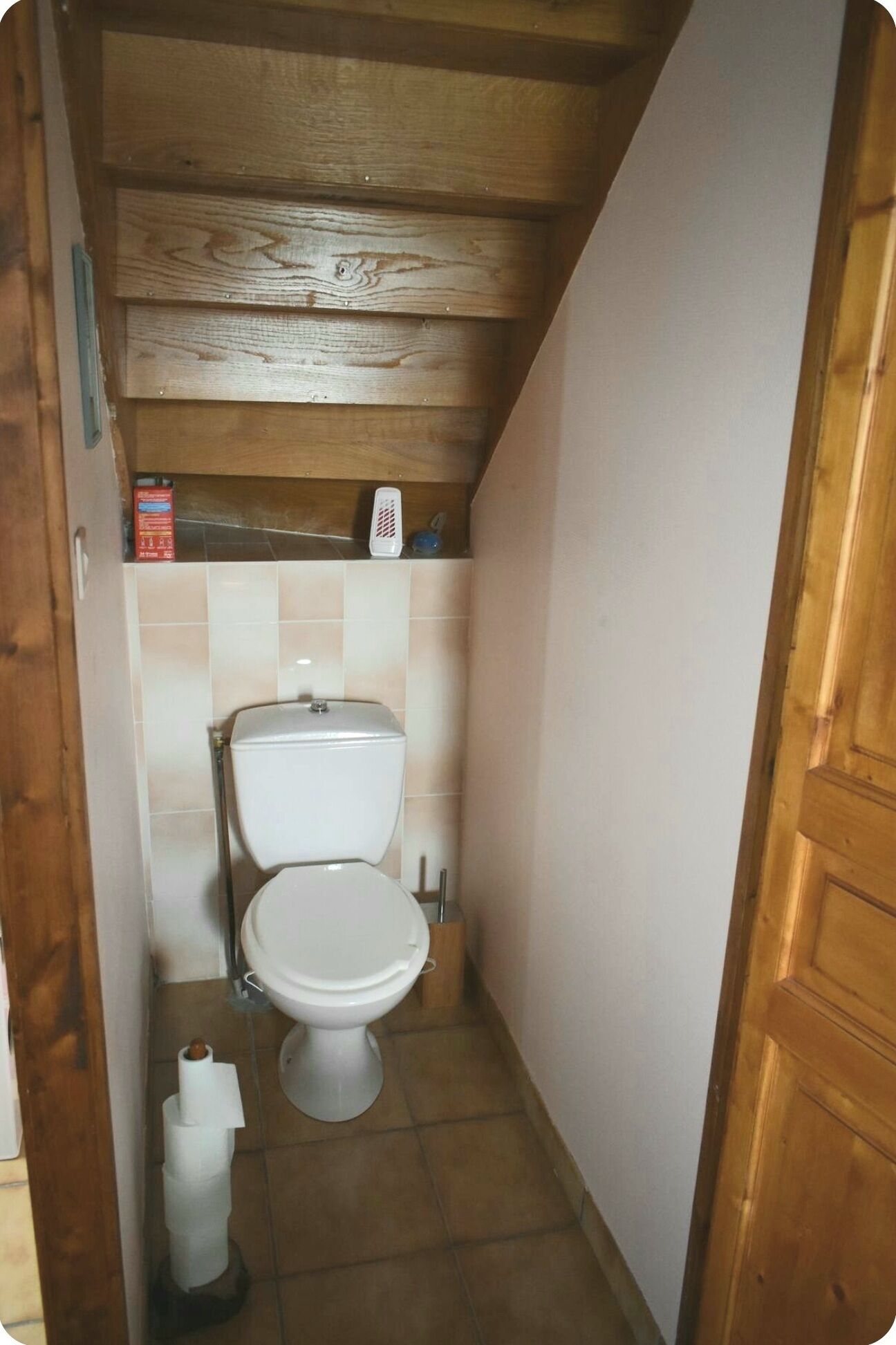 Un bagno piccolo e stretto con soffitto in legno, un water bianco e pavimento piastrellato.