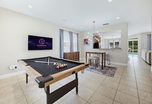 Mesa de bilhar em um quarto moderno com televisão, área de refeições e vista para uma piscina.
