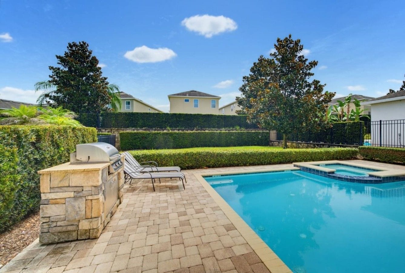 A swimming pool with a stone barbecue area and lounge chairs.