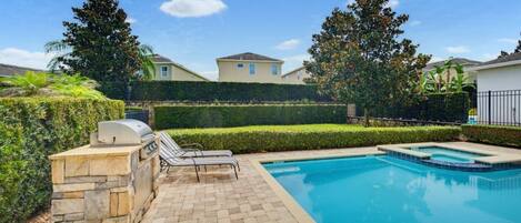 A swimming pool with a stone barbecue area and lounge chairs.