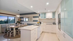 A modern kitchen with white cabinetry, a central island, and a dining area with a view.