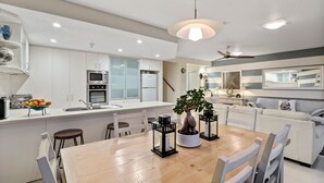 A modern kitchen with white cabinetry, a central island with a dining table, and a large window.