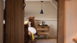 A bedroom with a bed, bedside table, lamp, and a wooden floor. - The Old Coach House (Alnwick)