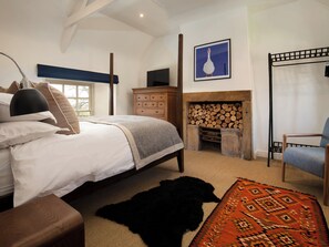 A bedroom with a bed, dresser, chair, fireplace, and a painting on the wall. - The Old Coach House (Alnwick)