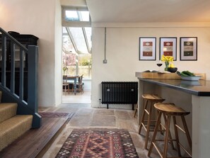 A modern kitchen with a bar area, a dining table with chairs, a radiator, and a staircase leading to another level. - The Old Coach House (Alnwick)