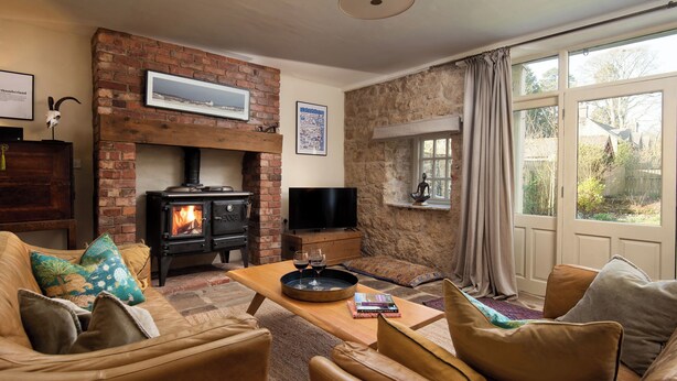 A cozy living room with a brick fireplace, leather sofas, and a television. - The Old Coach House (Alnwick)