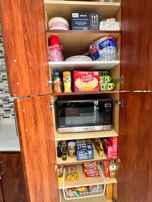 A kitchen pantry with storage shelves, a microwave, and various food items.