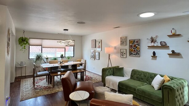 Un salon avec un canapé vert, un fauteuil en cuir marron et un coin repas comprenant une table et des chaises.