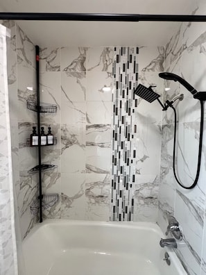 A modern bathroom with a marble-tiled shower wall, a black showerhead, and a chrome faucet.