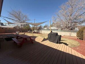 Una terraza de madera con mesas de picnic y una parrilla.