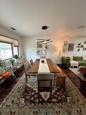A dining area with a wooden table, chairs, a patterned rug, and a hanging light fixture.