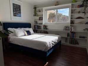 A bedroom with a bed, a window, and bookshelves. - Stardust Skies Retreat (Albuquerque)