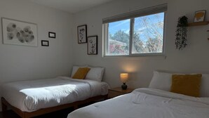 Une chambre avec deux lits, une fenêtre donnant sur la verdure et des œuvres d’art mural.