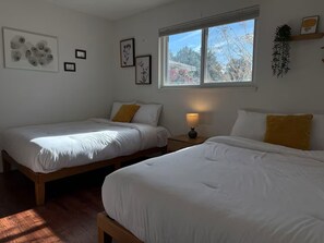 Une chambre avec deux lits, une fenêtre donnant sur la verdure et des œuvres d’art mural.
