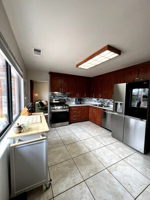 A modern kitchen with wooden cabinets, stainless steel appliances, and a large window.