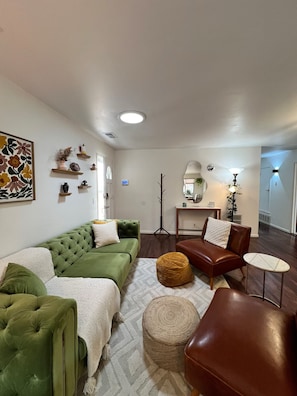 Un salon avec un canapé vert, un fauteuil en cuir marron, une petite table ronde et un miroir décoratif.
