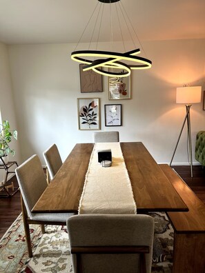 Un comedor con una mesa de madera, sillas, un tapete y obras de arte enmarcadas en la pared.