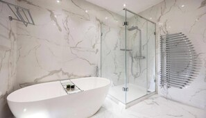 A modern bathroom with a freestanding bathtub, a glass-enclosed shower, and a marble wall. - Stylish Three-Bedroom Apartment in the Heart of Belsize Park (London)