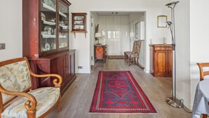 Ein geräumiges Zimmer mit einem Holzkabinent, einem gemusterten Sessel, einem roten Teppich und einer Stehlampe.