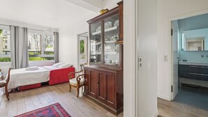 Ein Zimmer mit einem Bett, einer Holzkabine mit Glastüren, einem Badezimmer mit blau gefliesten Wänden und Blick ins Grüne.