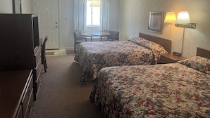 A hotel room with two beds, a desk, a chair, a lamp, and a TV.
