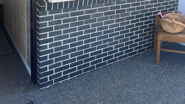 A reception desk with a brick facade, a glass window, and a wooden chair.